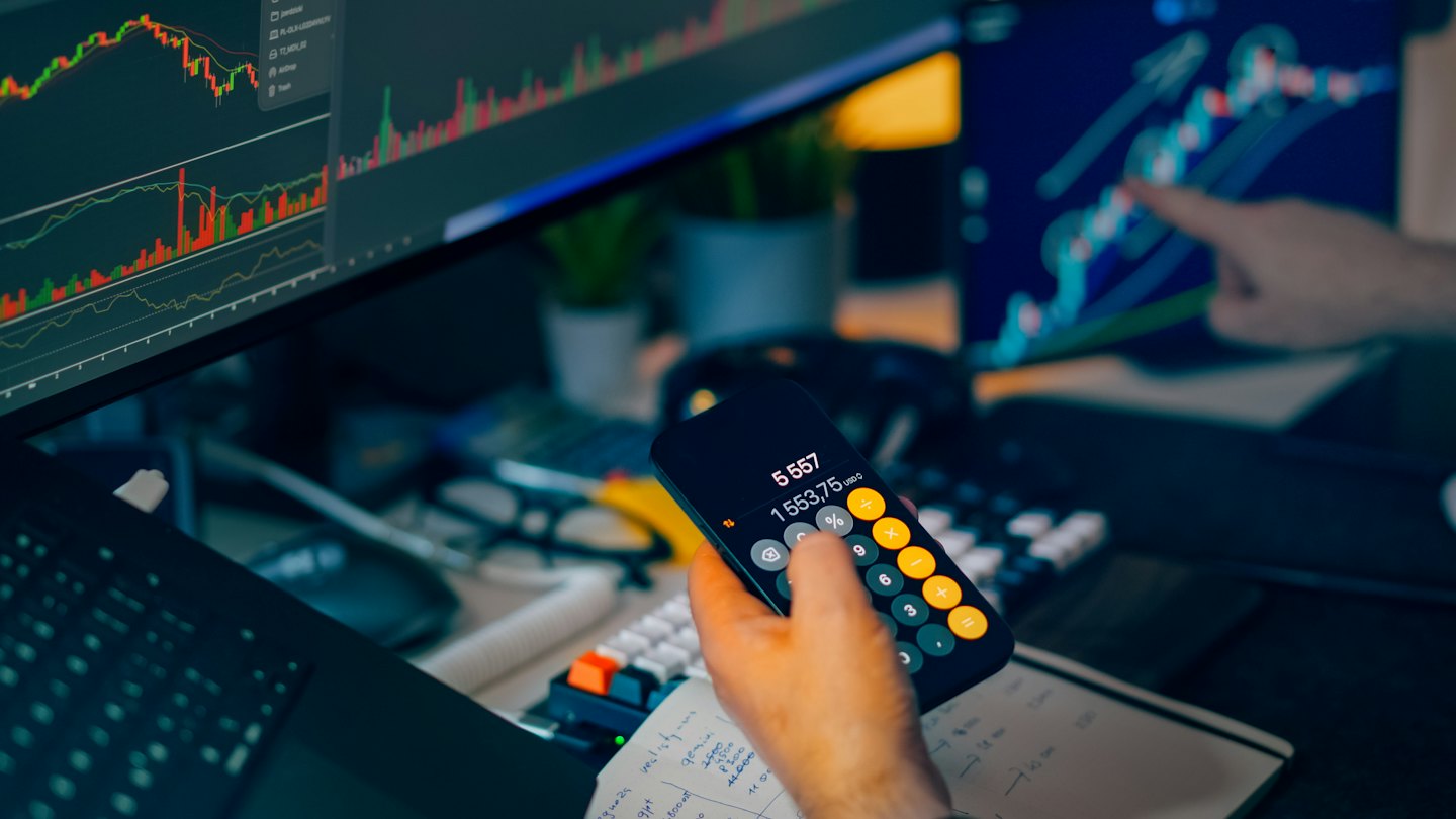 Hands hold a smartphone and point at stock market charts.